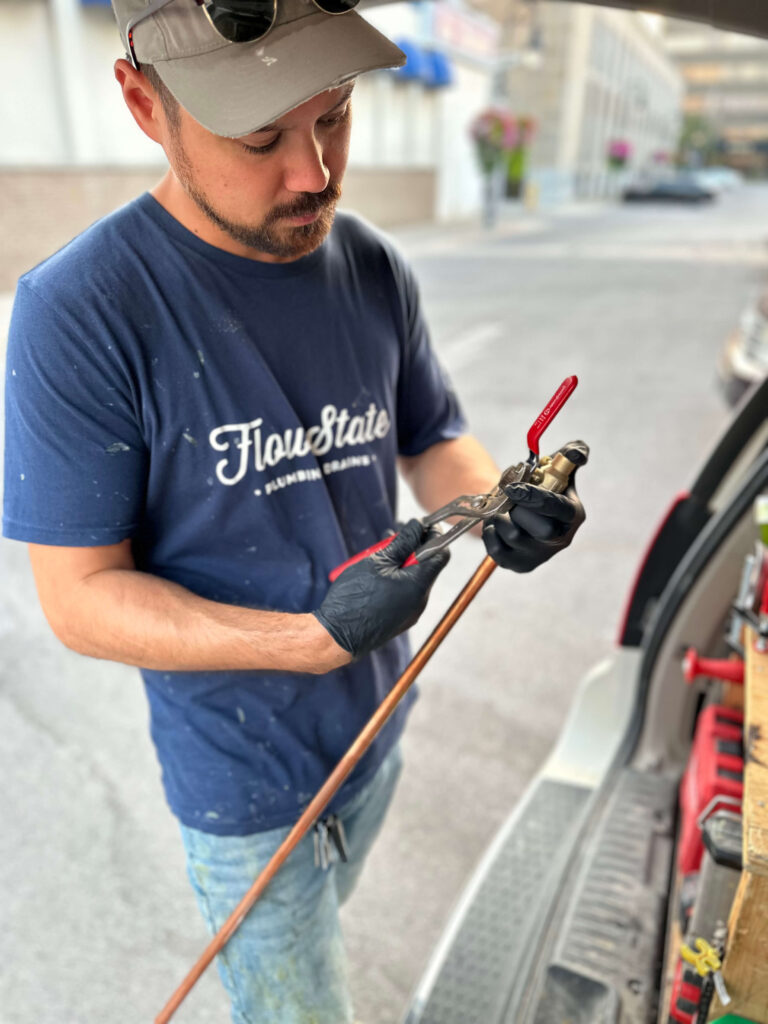 A niagara plumber adjusting a ball valve on a piece of copper pipe outside.