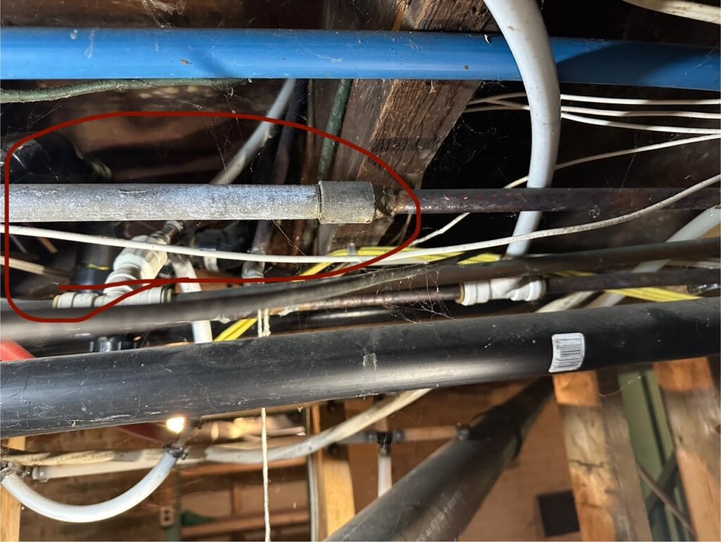 Old galvanized steel water pipe connection in a St. Catharines basement ceiling, surrounded by PEX, copper, and electrical wires.
