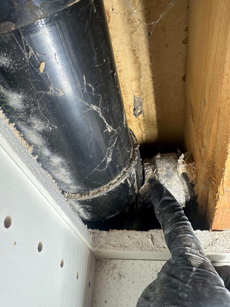 A niagara region plumber pointing to a broken drain pipe inside a wall that is leaking water and waste.