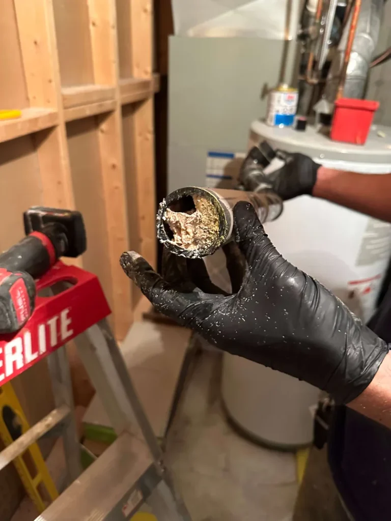 A plumber holding a cut inch and a half kitchen drain pipe clogged with kitchen grease during an emergency plumbing call.