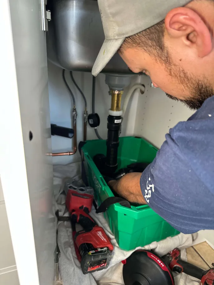 Close-up of Flow State Plumbing technician organizing ABS fittings during a kitchen drain repair, with Milwaukee power tools and copper stub-outs in view.