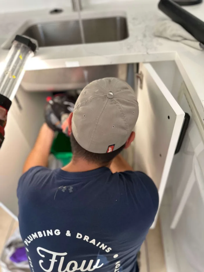 Flow State plumber crouched under a kitchen sink in Niagara Region, performing drain cleaning with tools and flashlight visible.