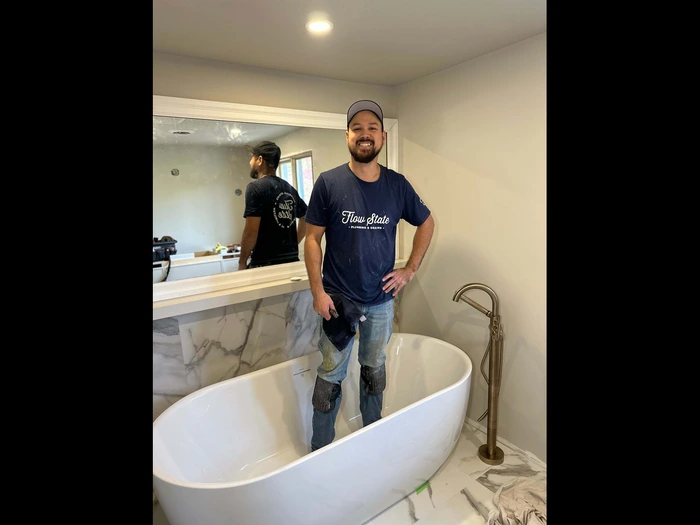 A St Catharines plumber smiling, standing inside a newly installed free standing bath tub.