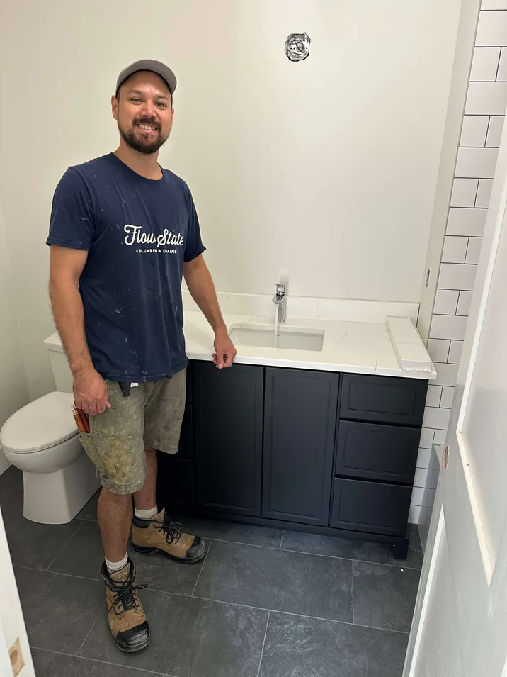 A smiling Niagara region plumber standing in newly finished bathroom with a freshly installed toilet and vanity.