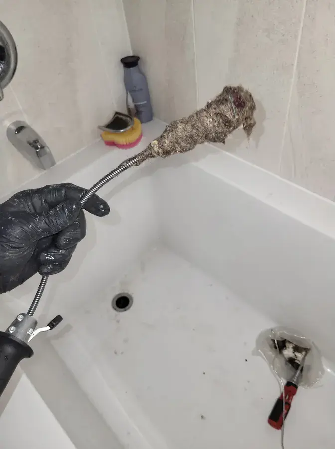 A Niagara Falls plumber holding a drain snake tool with a big ball of hair taken from a clogged shower