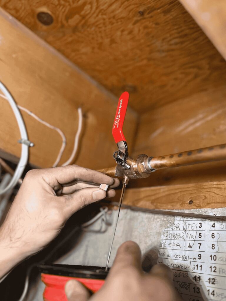 A plumber with an opened drain cap on an indoor water valve draining water from outdoor spigot (aka, hose bib)