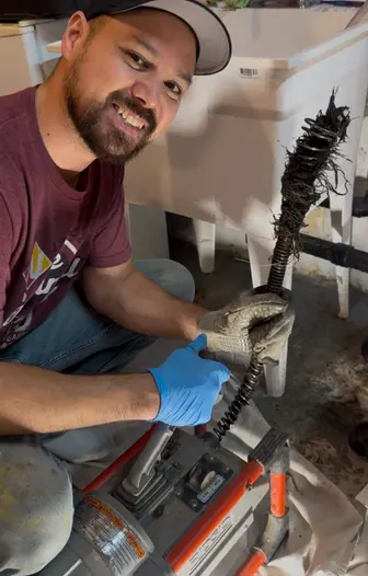A thorold plumber smiling at camera holding a drain cleaning machine that has tree roots from a customers main drain line