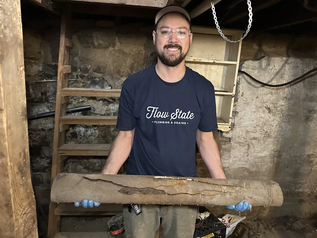 A plumber smiling holding a length of cracked cast iron drain pipe in a sewer line repair job